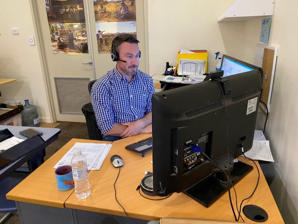A worker sits at his desk at Voyages Indigenous Tourism office wearing headset and blue check shirt sitting in front of a computer screen