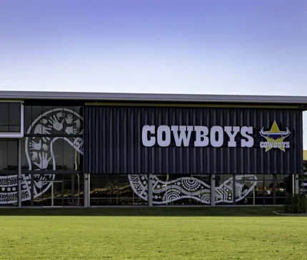 NQ Cowboys Community Training and High-Performance centre Front View Of Exterior With Indigenous Snake Artwork On Glass And Cowboys Logo With Grass In The Foreground on Hutchinson Builders Centre