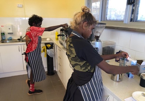 Two Indigenous trainees practice making coffee in a kitchen